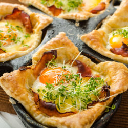 Fried eggs in puff pastry in ham, baked with cheese and topped with microgreens, fresh juice from oranges and eggs stuffed with chocolate